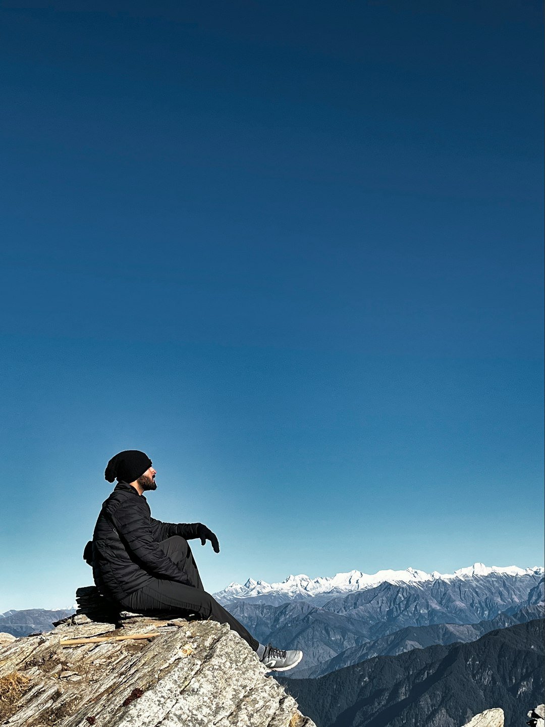 A person sitting on top of a rock on top of a mountain