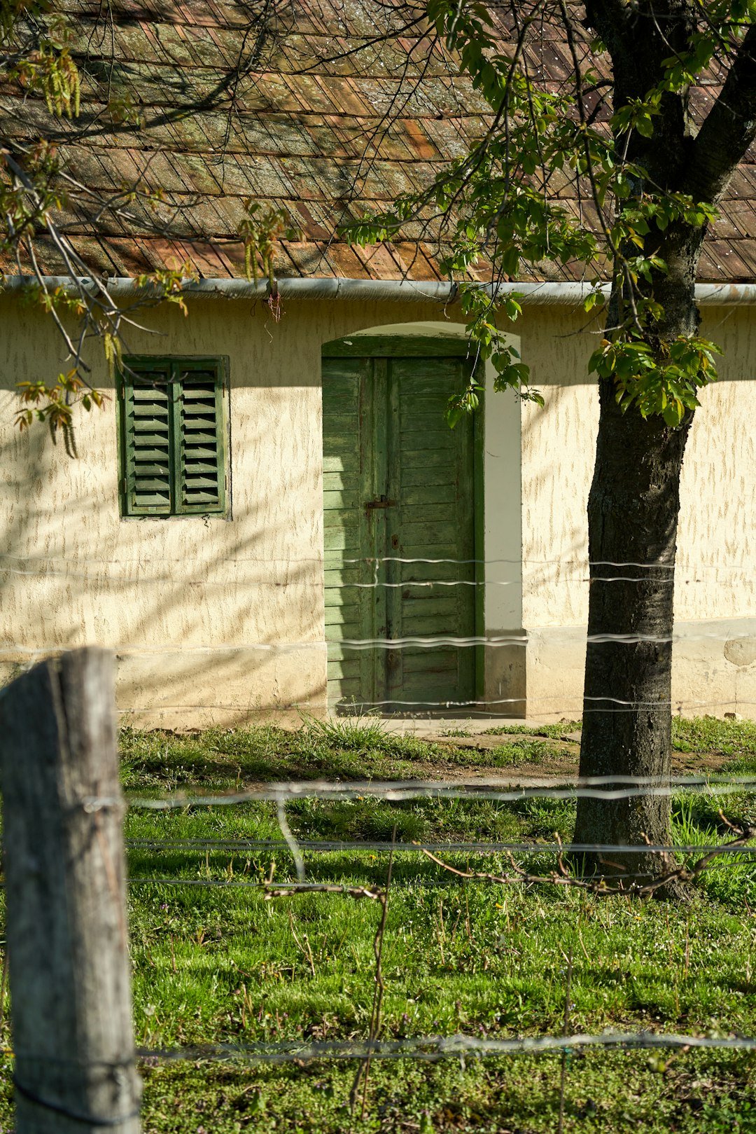 An old building stands behind a barbed wire fence.