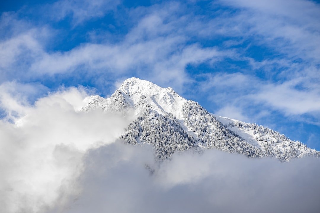 a mountain covered in snow and clouds under a blue sky