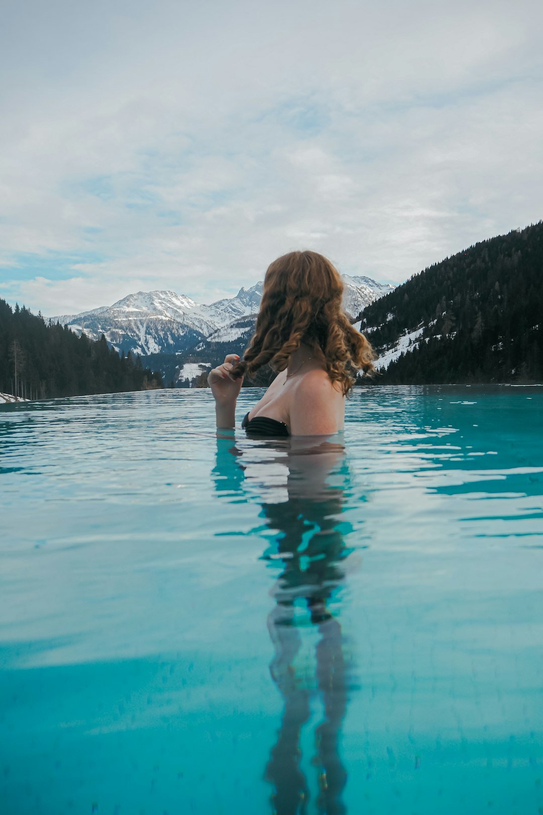 a woman sitting in a pool of water with mountains in the background