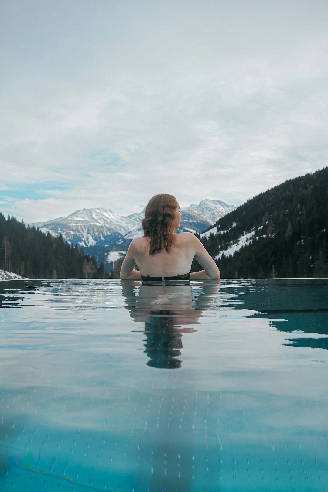 a woman sitting in a pool of water with mountains in the background