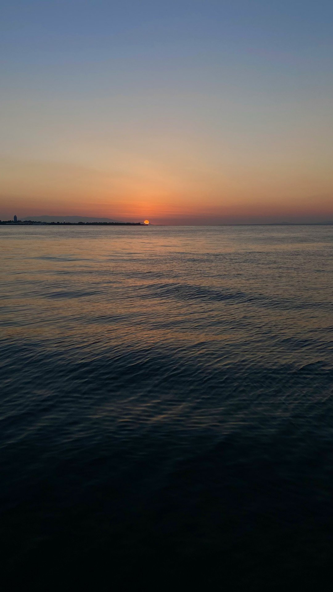the sun is setting over the ocean with a boat in the distance
