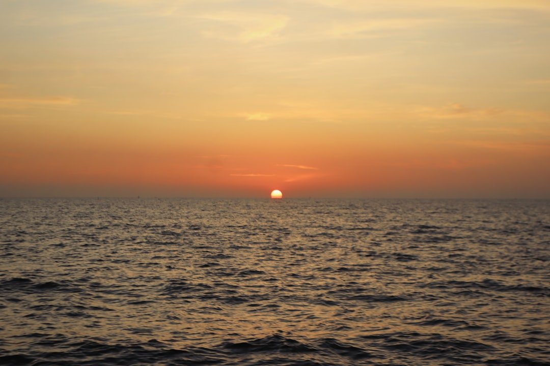 The sun is setting over the ocean on a cloudy day