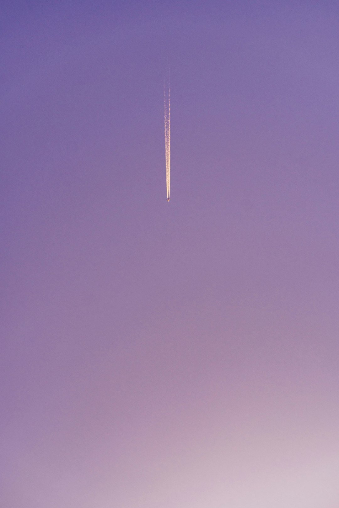A plane leaves a trail in the purple sky.