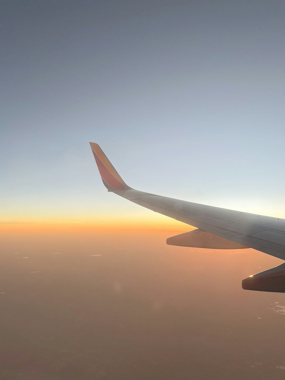 Airplane wing soaring through a sunset sky.