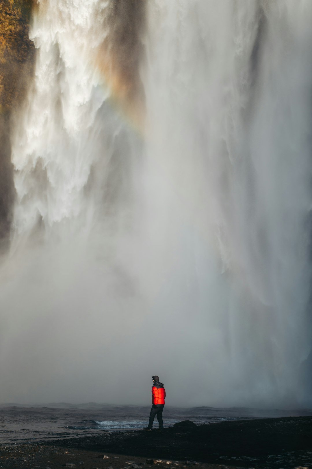 a man standing in front of a waterfall with a rainbow in the background
